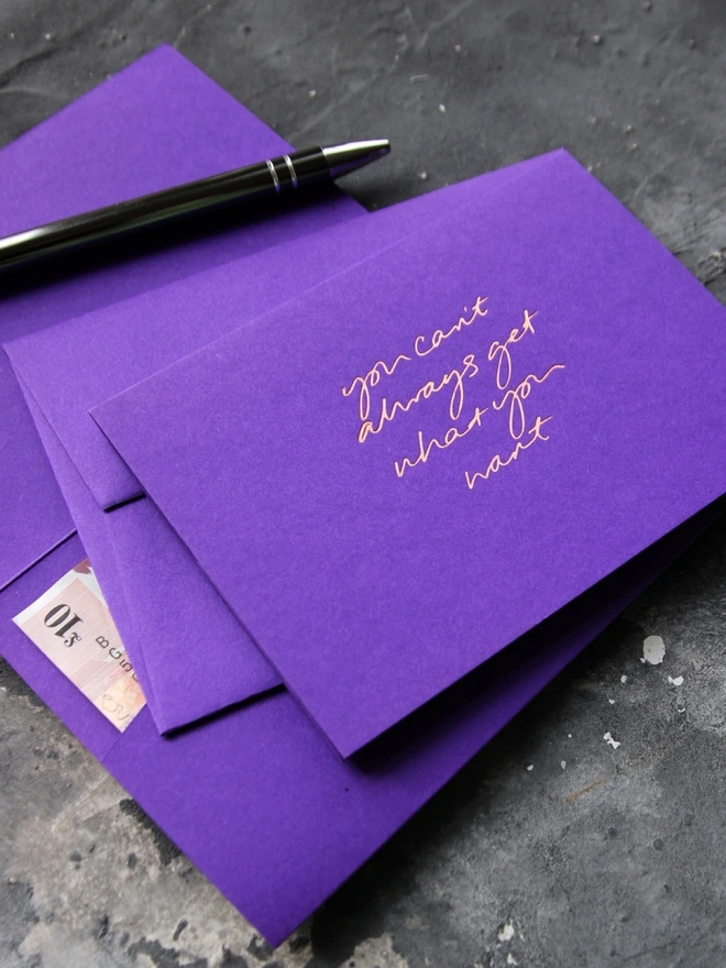 Hand foiled cash card or money wallet in a royal purple colour handfoiled in shiny rose gold foil text which says ‘You Can’t Always Get What You Want’.