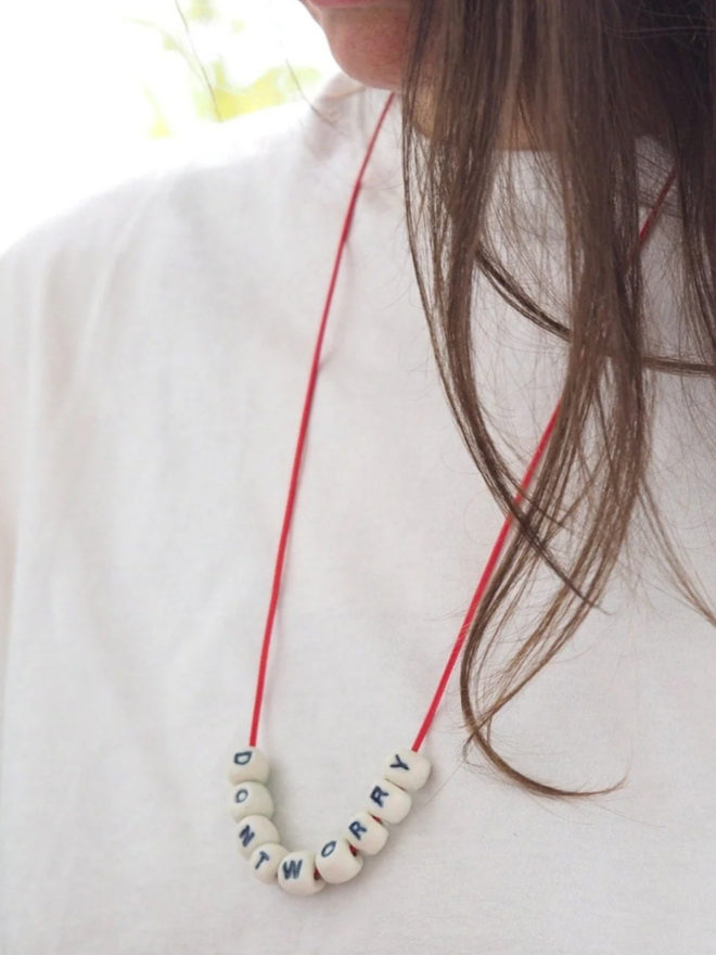 Don’t Worry Necklace. A woman wearing a necklace which reads DON’T WORRY in porcelain beads.