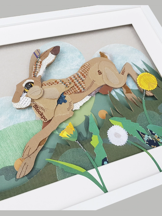 Hare leaping through long grass and dandelions, created using multiple layers of corrugated card, decorated with salvaged fabric and paper. Including buttons and feathers. Finished off with machine and hand embroidery.  
