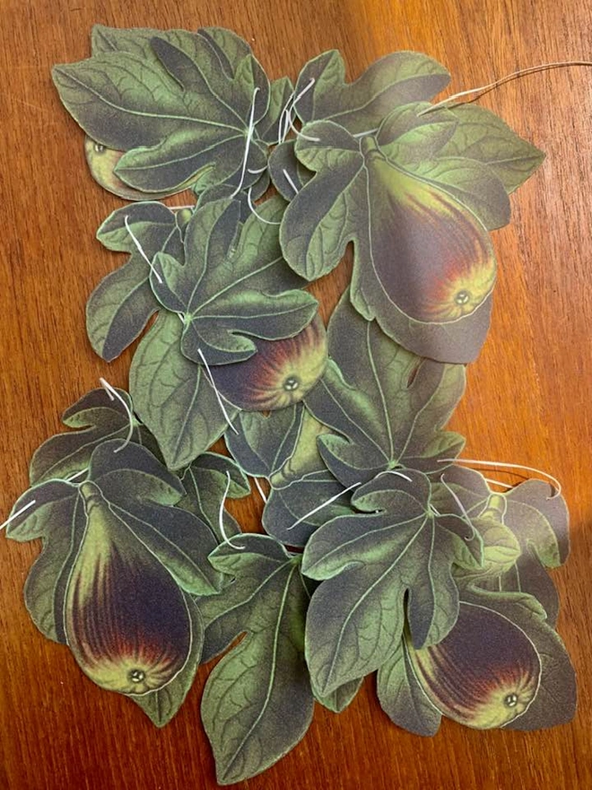 A bundle of bunting featuring figs and fig leaves in greens and browns on a teak table