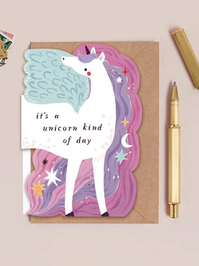Unicorn Birthday Card reading it's a unicorn kind of day, with a kraft envelope and a gold pen