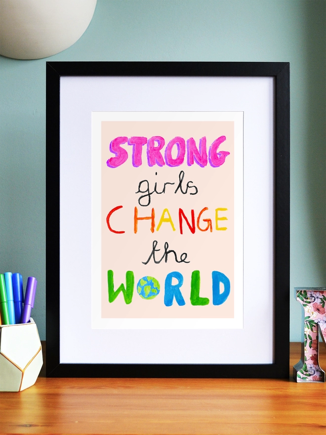 Art print saying 'Strong girls change the world' in a black frame in a child's room