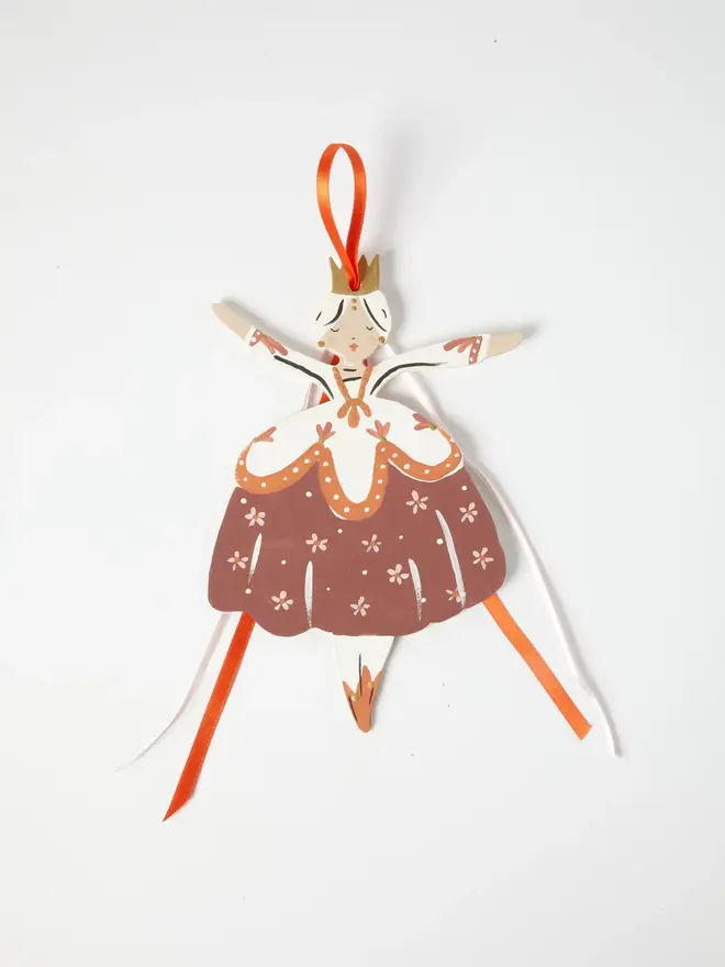Belle Tree Dancer. wooden hanging ballerina decoration with a gold crown, cream bodice and terracotta floral skirt, orange and white ribbon ties, arms outstretched, on a white background