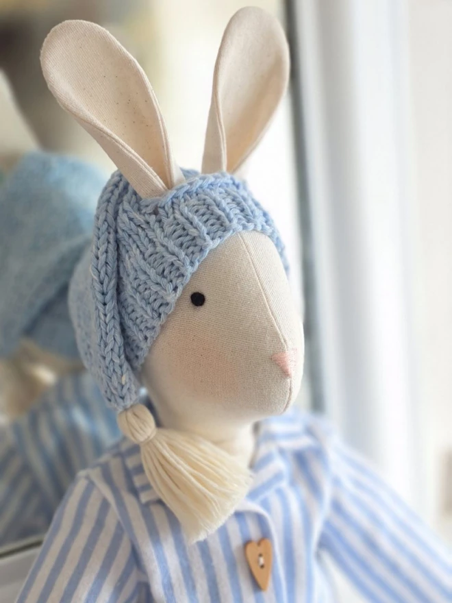 Close-up of handmade linen Gerald Bunny wearing blue striped Christmas pyjamas and a pale blue hand-knitted sleepy hat with tassel.