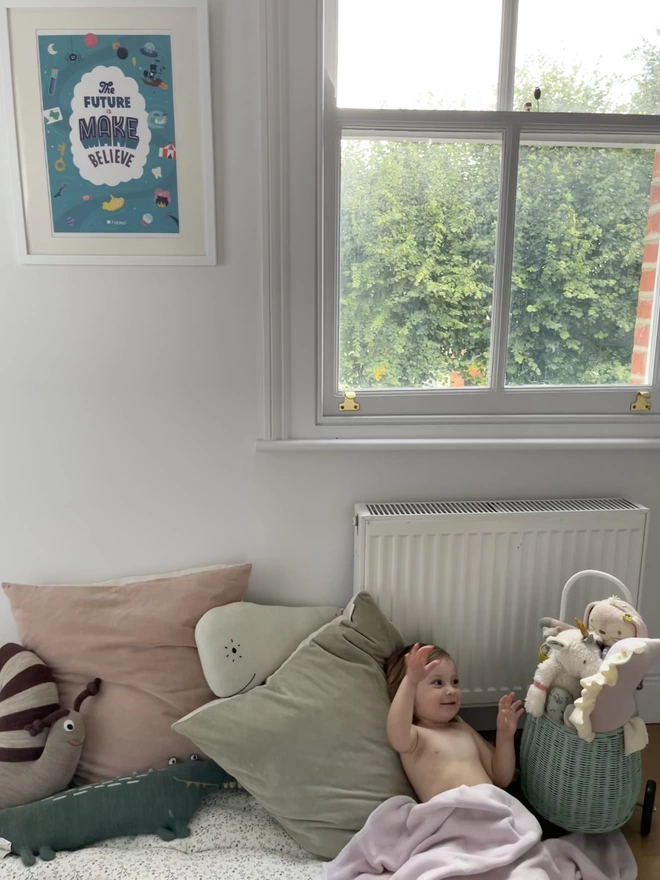 Bright poster hanging on wall in nursery with baby playing on cushions