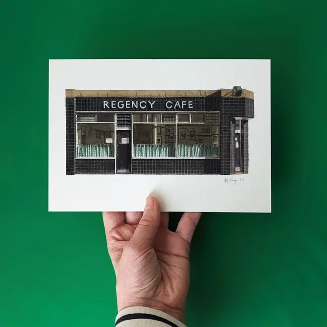 Pimlico Regency Cafe Giclée Print (Unframed) Victoria, a print of a cafe held in front of a green backdrop by a person. 