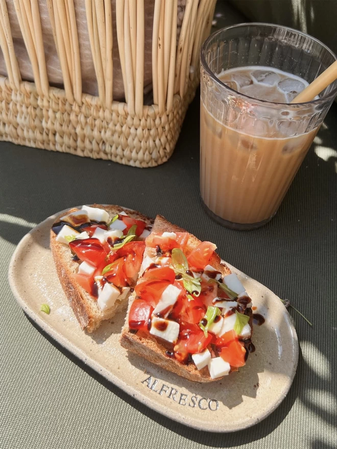 2 slices of bruschetta sat on a beige, oval plate with the word 'alfresco' stamped around the edge