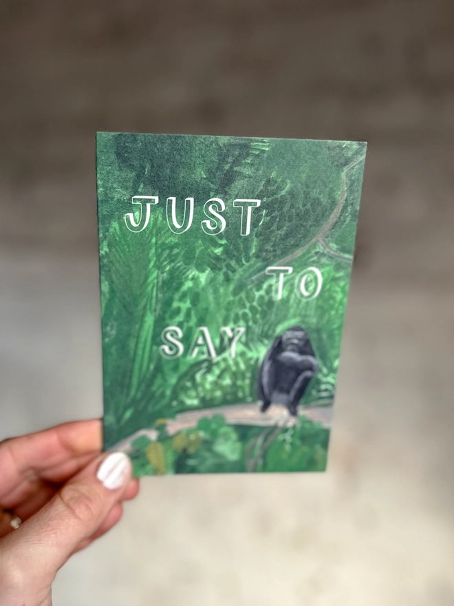 a greetings card featuring an illustration of a chimp sitting in the jungle with the text “just to say”