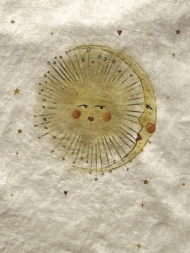 'Astral Weeks' Linen Tea Towel, a print sitting on a wooden surface with a sun motif in the centre. 