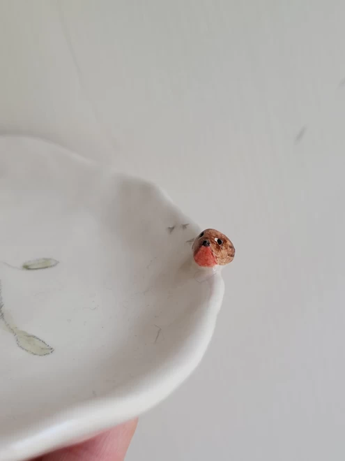 close up of front view of a ceramic robin figurine with red breast attached to the rim of a white earthenware soap dish  