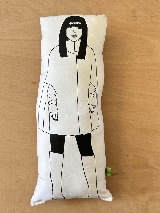 Black and white illustrated screen printed cushion of Traitors host Claudia Winkleman. The cushion sits on a light wood surface.