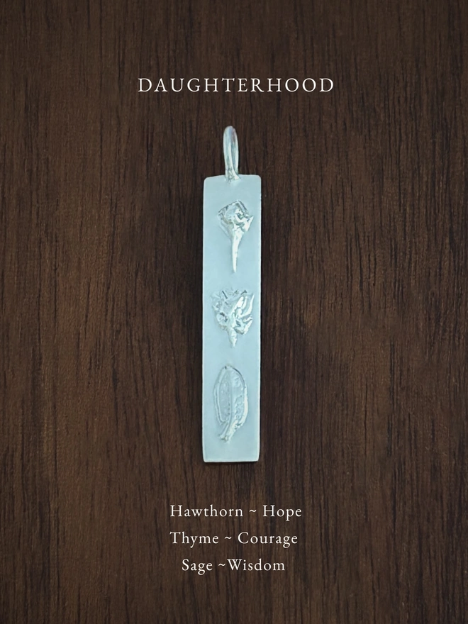 Daughterhood bar pendant in sterling silver on a dark background with the meaning of the flowers written in white