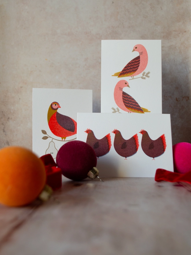 Bright and colourful, 3 maximalist feeling mini Christmas cards featuring partridge in a pear tree, two turtle doves and 3 French hens are stacked with jewel toned Christmas baubles and ribbons surrounding them