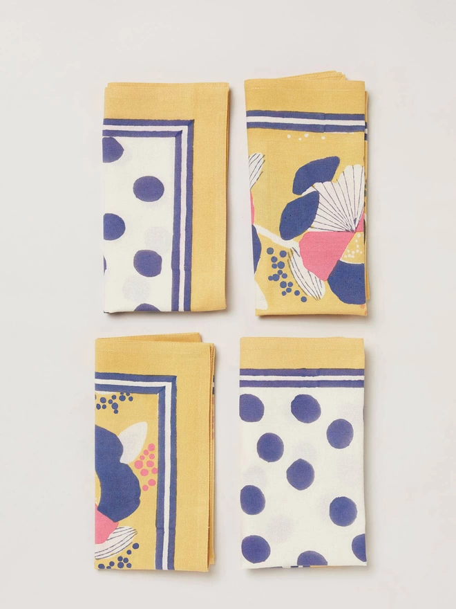 Set of 4 napkins, two featuring block printed yellow floral design and two in a block printed navy spot