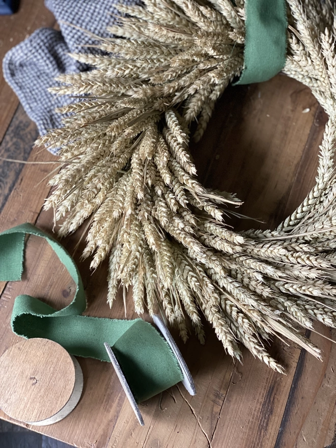 A handmade September Harvest Wheat Wreath with a sage green ribbon looped around the top and trailing by its side
