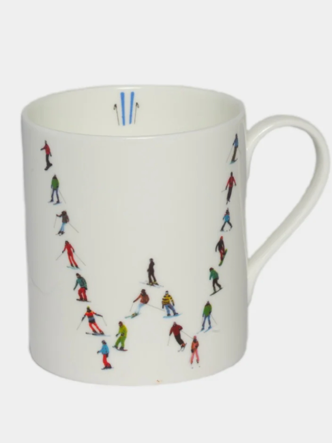 A simple white mug illustrated with a ‘W’ made of small, multicoloured skiers. The mug is set against a plain, white background.