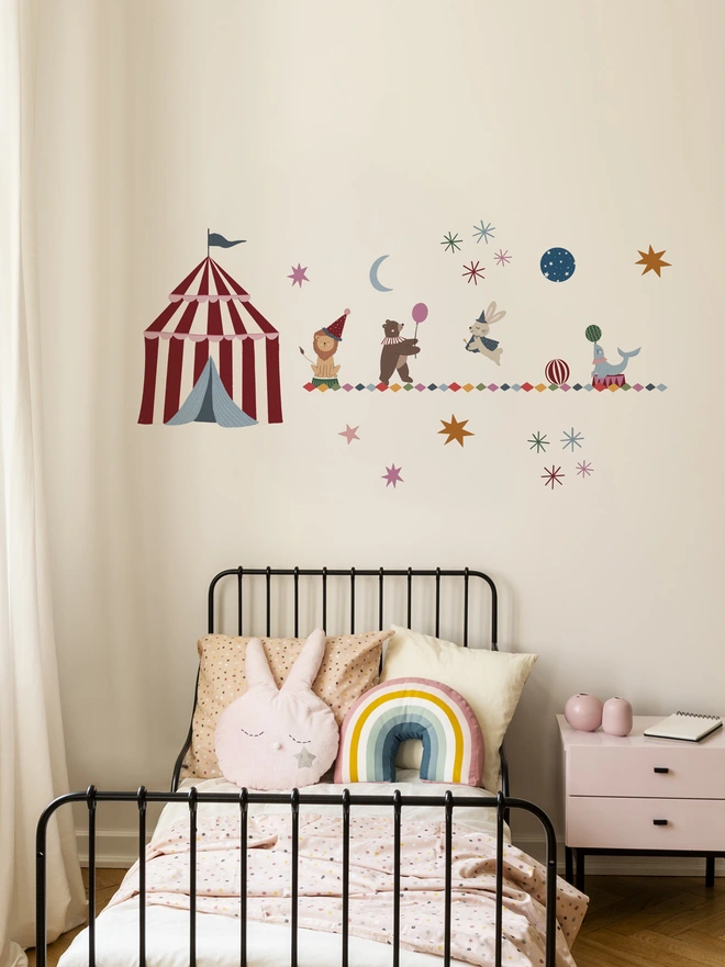 White wall with circus tent, lion, bear, rabbit and seal wall stickers above a black metal framed bed