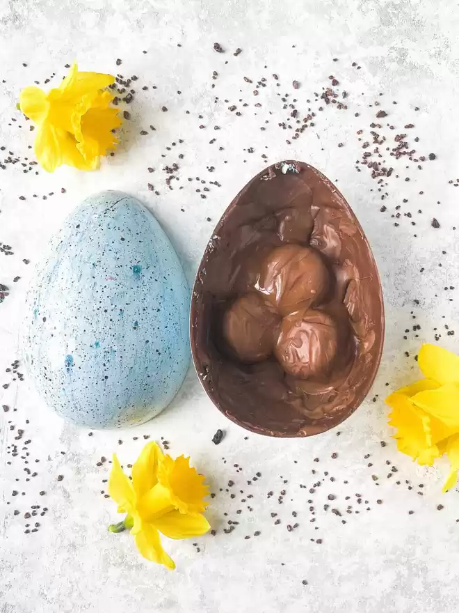 a blue speckled easter egg sitting on top of a blue background with a half open egg showing chocolate covered macarons embedded inside
