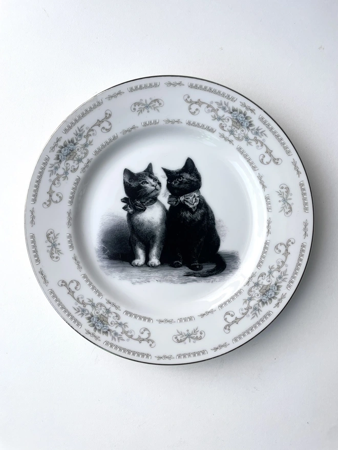 a vintage plate with an ornate border, in the centre of the plate is a vintage style black and white illustration of a black witch's cat