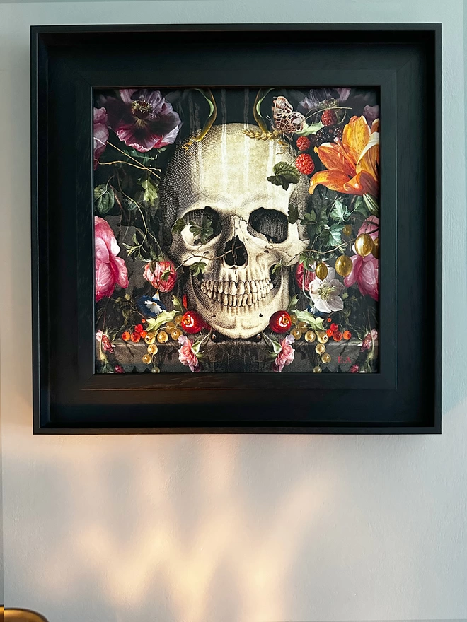 Close up of framed Memento Mori Skull and floral artwork in black frame hanging in the home