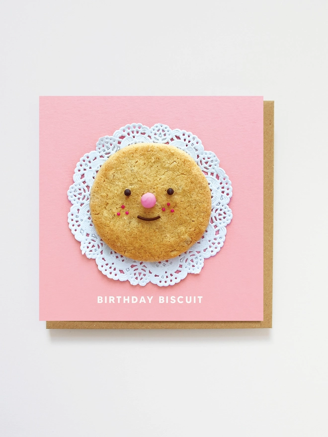 A birthday biscuit with a cute face sitting on a doiley 