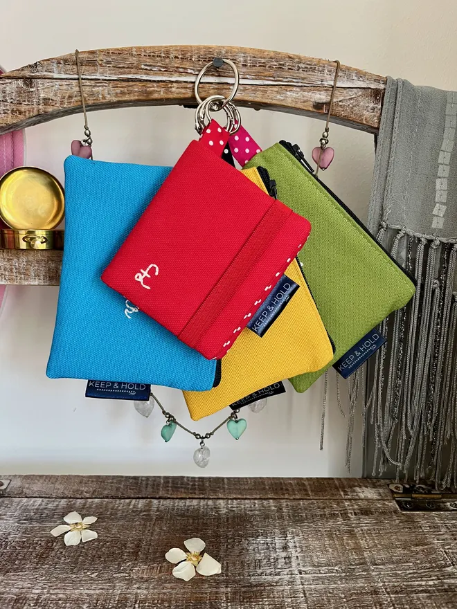Set of 3 brightly coloured coin purses and 1 card wallet hanging on a stand.