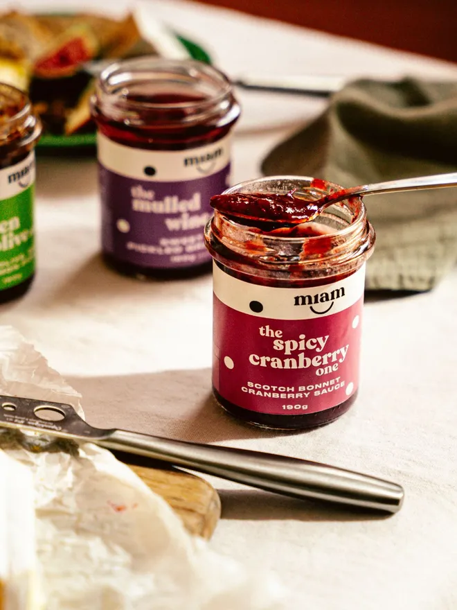 Spicy cranberry sauce in a jar with a spoon on a wooden board with cream-coloured cloth