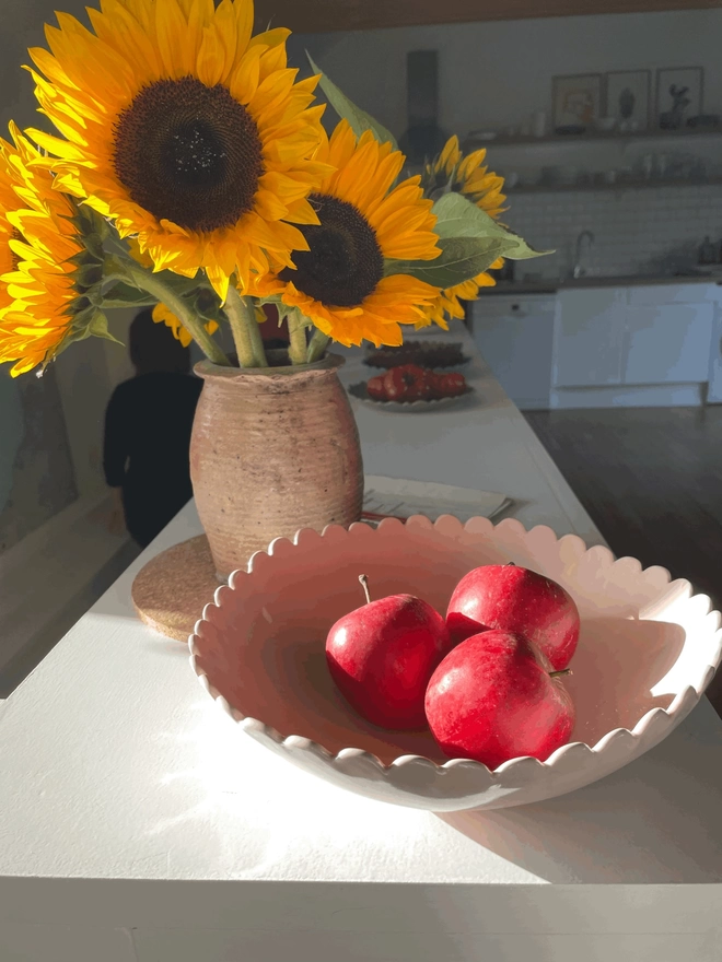 apples in a blossom pink scalloped edge fruit bowl with sunflowers in a vase