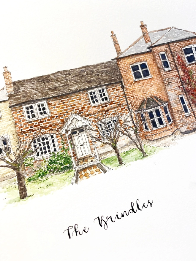 Close up showing a white page inside and a beautiful mixed historic style house in the centre painted in intricate watercolour details. Below black calligraphy lettering reads The Brindles