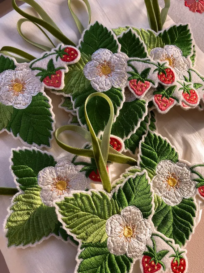 Collection of embroidered strawberry and blossom hanging decorations with green velvet ribbons.