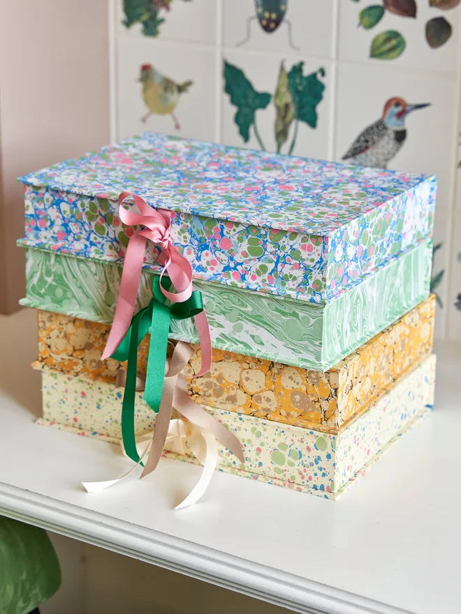 stack of four keepsake boxes. each box is hand marbled in a different pattern/colour and has a ribbon tie closure