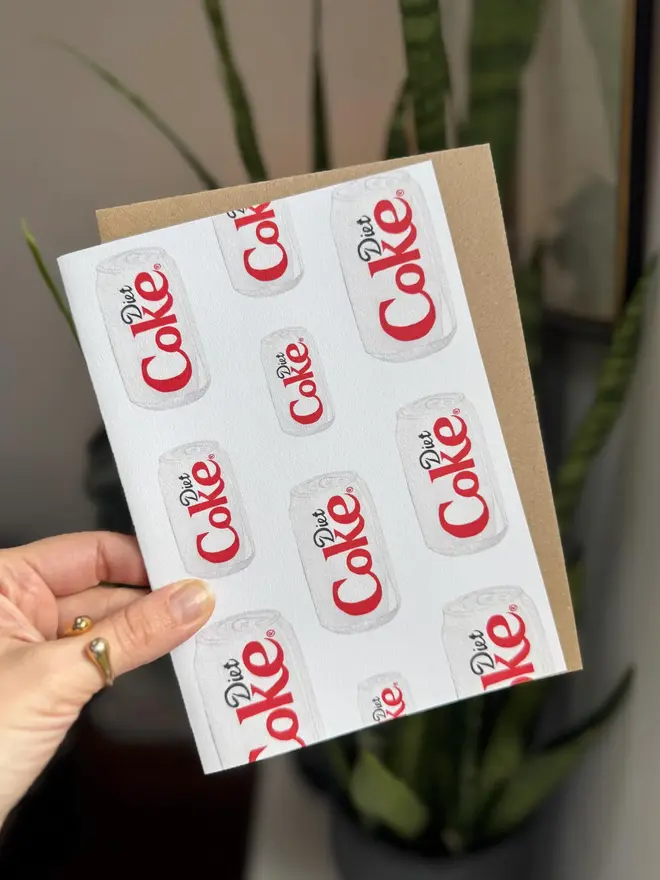 diet coke cans illustrated card. card photographed inside with houseplant in background.