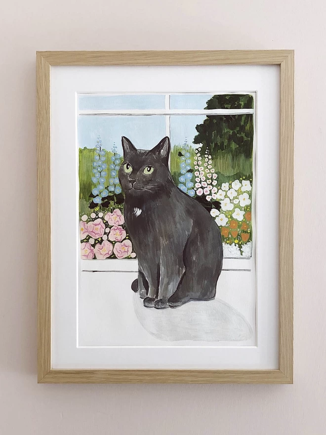 A beautiful grey cat with green eyes sitting on a windowsill. Through the window behind the cat there is an illustrated cottage garden, with delphiniums in blues, pinks and white.