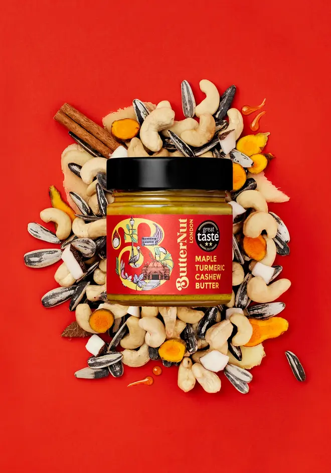 Maple Turmeric Cashew Butter against a red background styled with nuts and spices