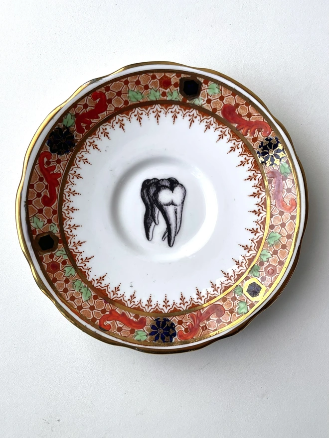 vintage plate with ornate border has a black and white image of a victorian molar tooth in the centre