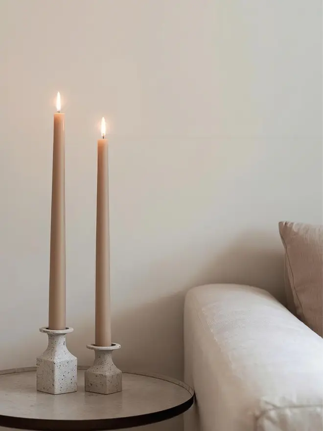 Two latte dinner candles in candle holders on a side table next to a sofa