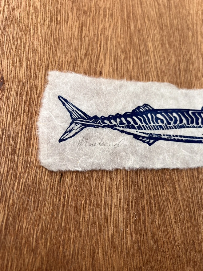 Close-up of a hand-printed mackerel lino print showing the carved lines, ink texture and natural grain of the handmade paper.