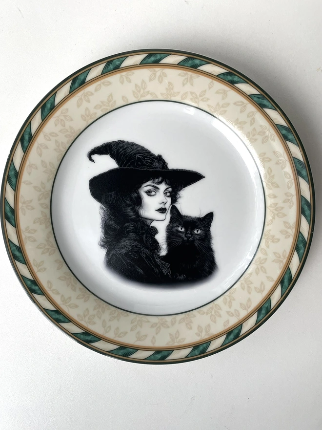 vintage plate with an ornate border, with a printed vintage illustration of a Victorian witch and her black cat in the middle