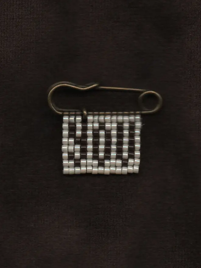 'linga viii' beaded 'you' pin. a pin badge with the word you in brown lettering against a pearl background.