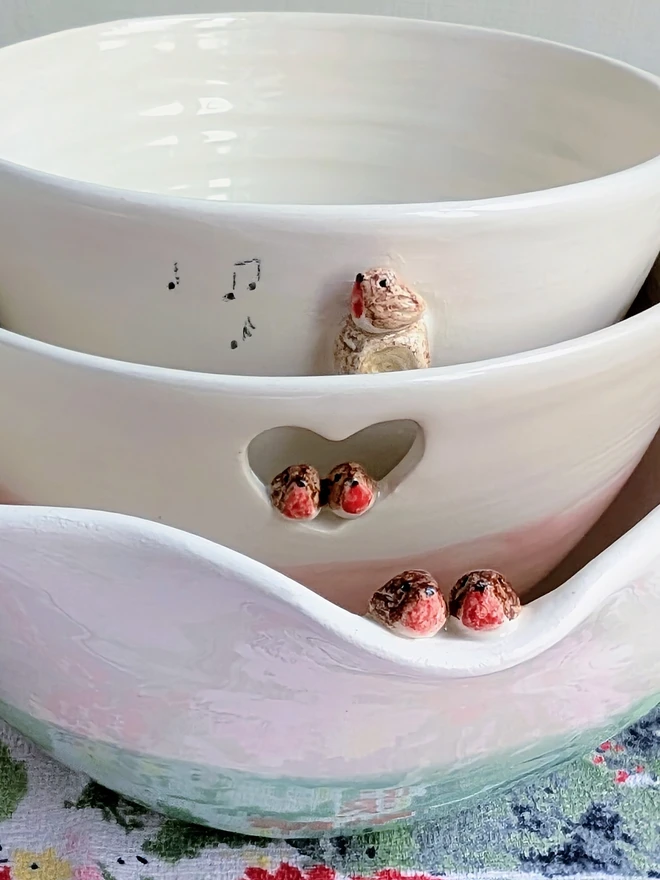 white ceramic bowl with a tiny modelled robin perching on a modelled branch with musical notes, the bowl is nesting in a larger pink robin couple bowl