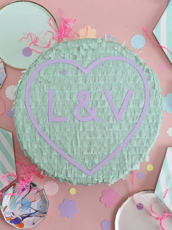 mint love heart pinata with initials inside in lilac surrounded by confetti and paper plates