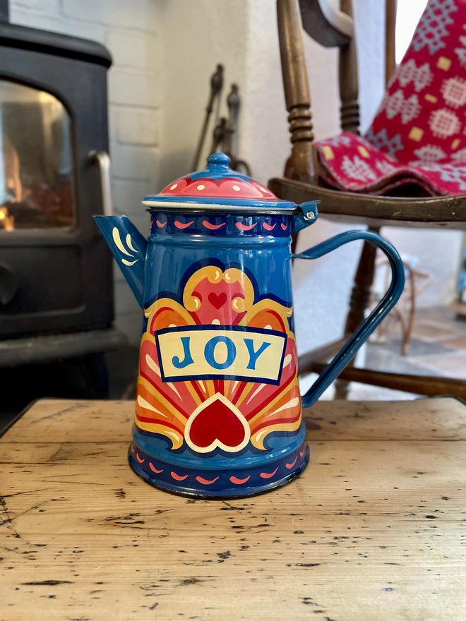 Blue vintage coffee pot, hand painted with a fairground inspired design in pink, orange and yellow. 'Joy' is painted in a banner through the centre of the design.