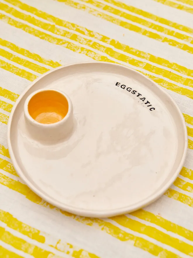 Egg And Soldier Plates, a plate with an integrated egg cup placed on a yellow striped surface. The wording reads 'eggtastic' 