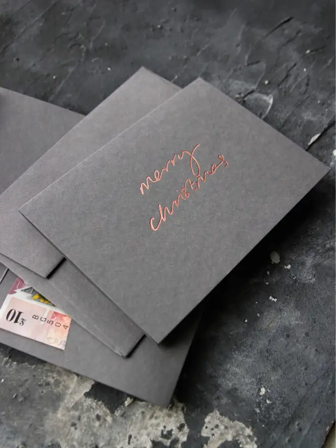 Hand foiled cash card or money wallet in a smoke grey colour in shiny bronze foil text which says ‘merry christmas’.