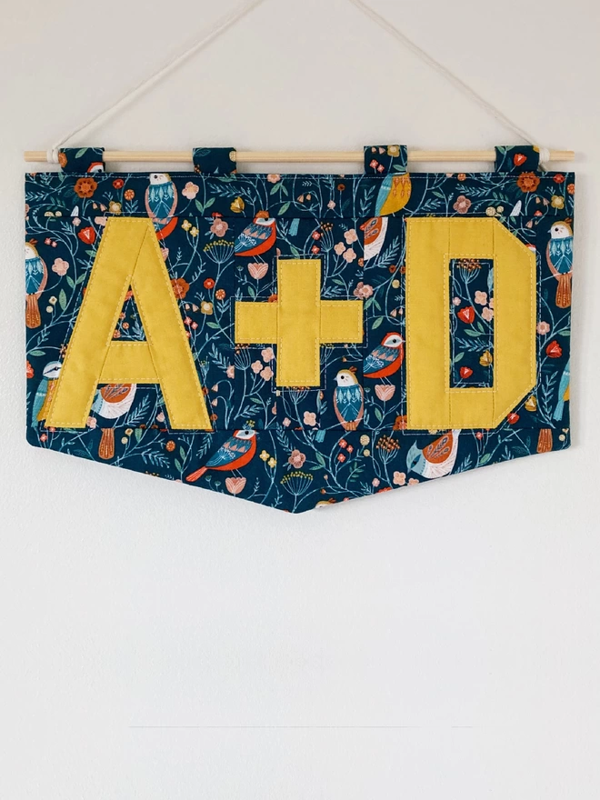 Cooper and Fred personalised quilted double letter wall hanging using a blue pattern with birds and plants and yellow lettering.