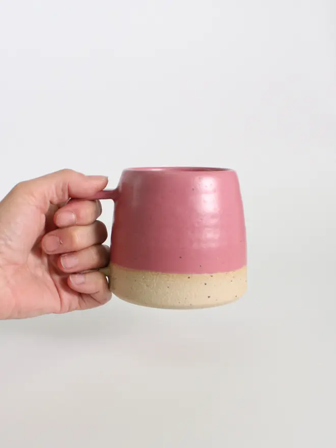 Hand holding our handmade ceramic fuchsia mug against a white background.
