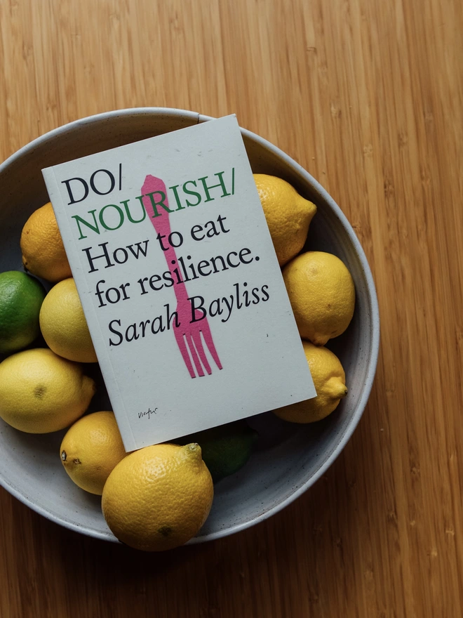 Book resting in bowl of lemons and limes on a wooden surface