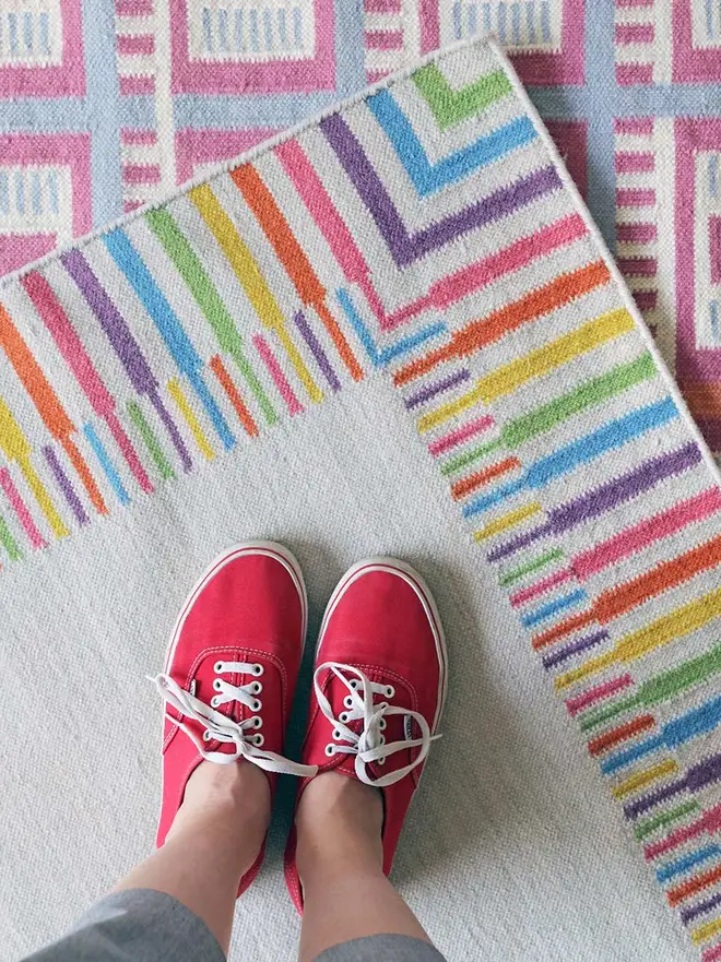 Rainbow Border Flatweave Rug, a rainbow rug sitting underneath a pair of red shoes. 