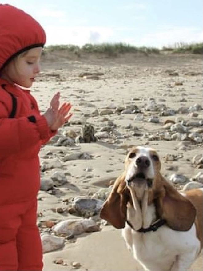 Piper as a 6 year old in a red snowsuit on the beach with her pet bunty who was a basset hound