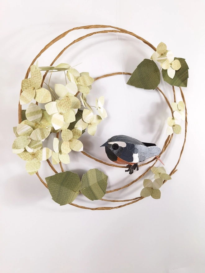 handmade paper sculpture of a redstart bird, perched on a wreath of green hydrangea blooms